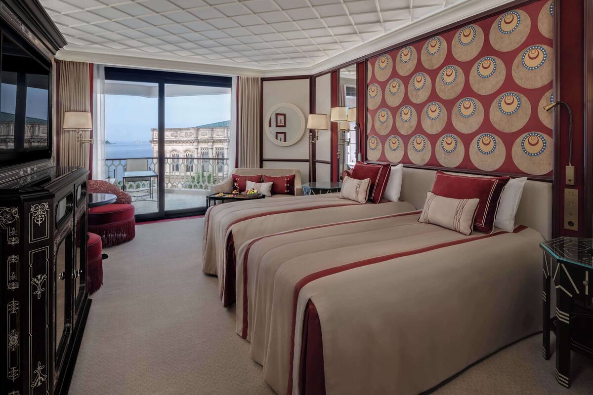 A hotel room with two beds, a large window with a view of a historic building, and a balcony.