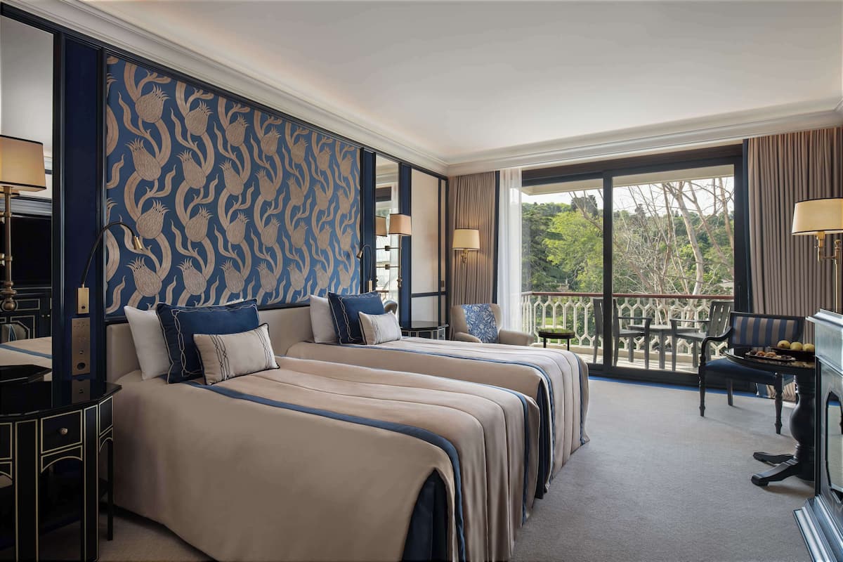 A hotel room with two beds, a balcony with a view, and a desk with a lamp.