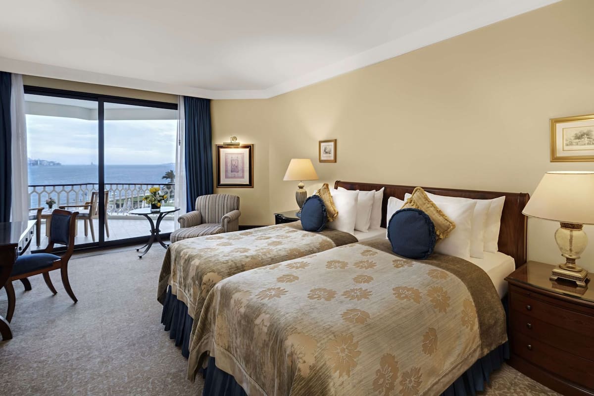 A hotel room with two beds, a balcony with a view, a small table with chairs, and a desk.