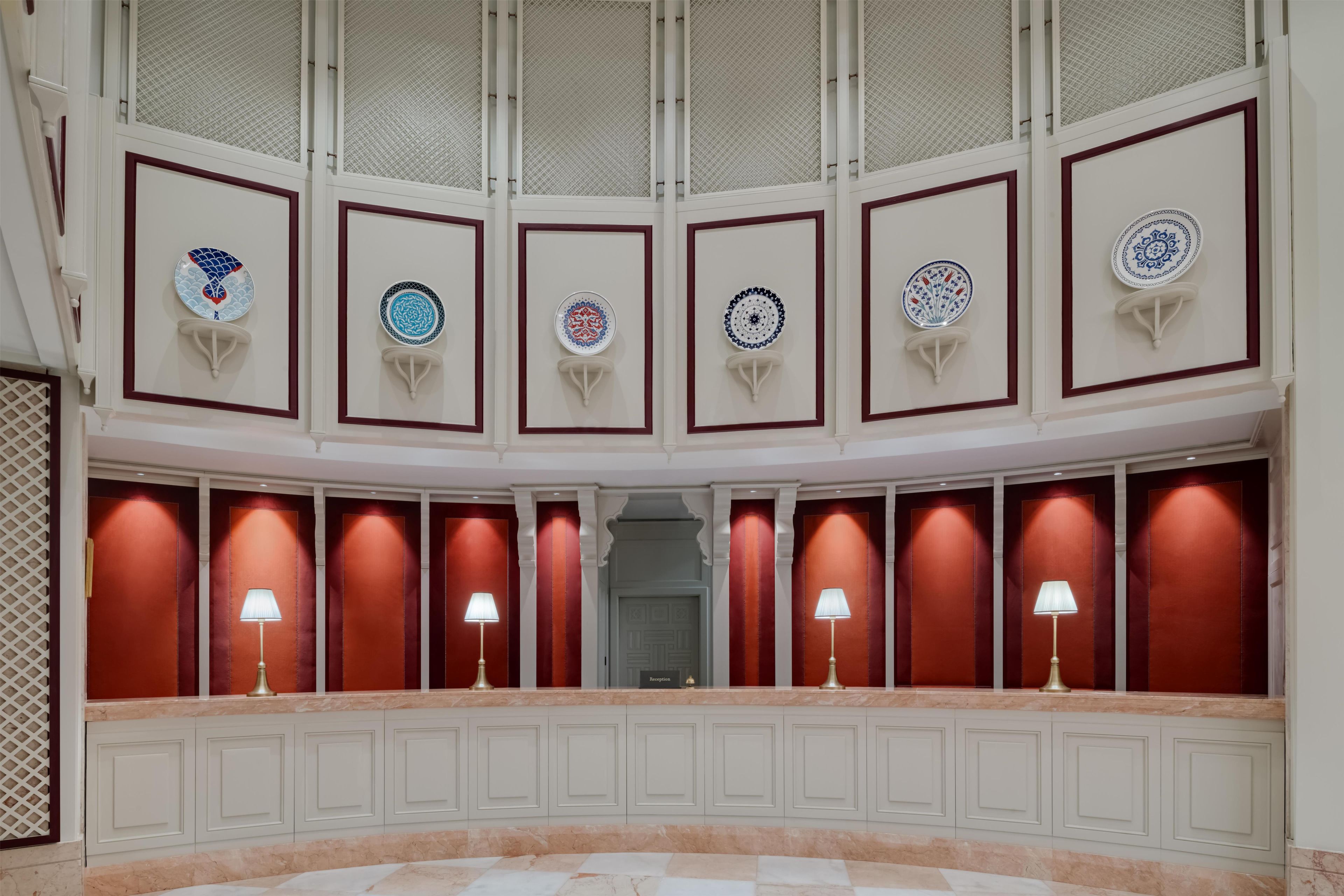 A reception area with a curved wall displaying decorative plates, a marble floor, and a reception desk with lamps.