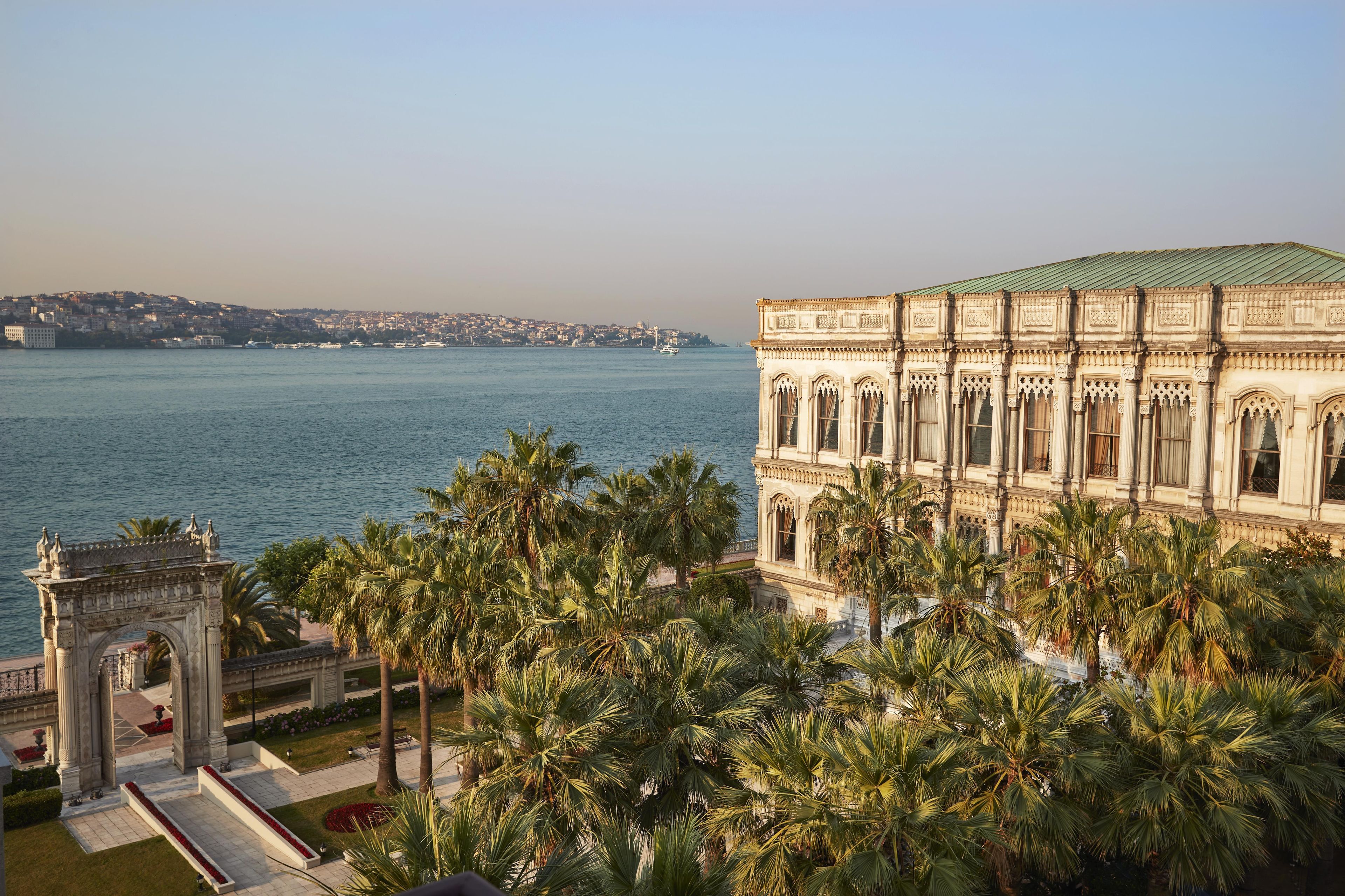 A waterfront building with classical architecture, a port with boats, and a cityscape in the background.