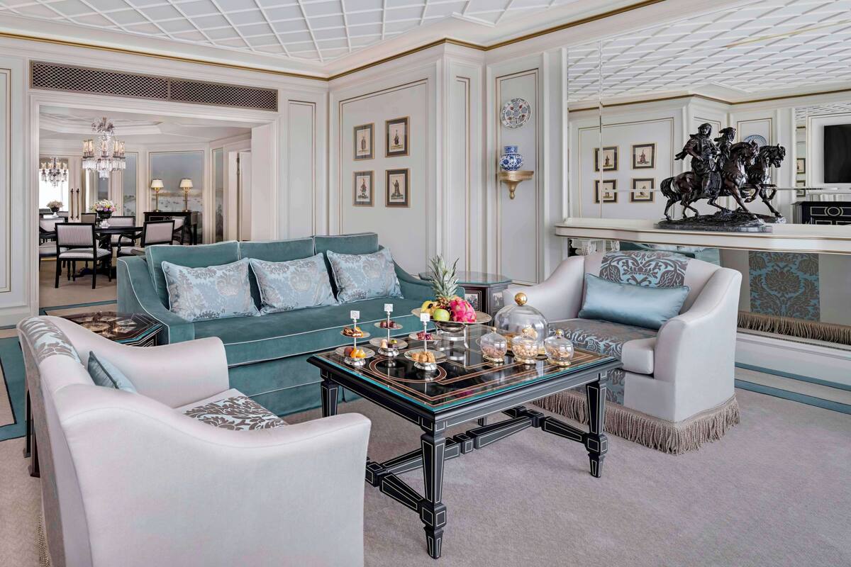 A spacious living room with a teal sofa, white armchairs, and a glass coffee table.