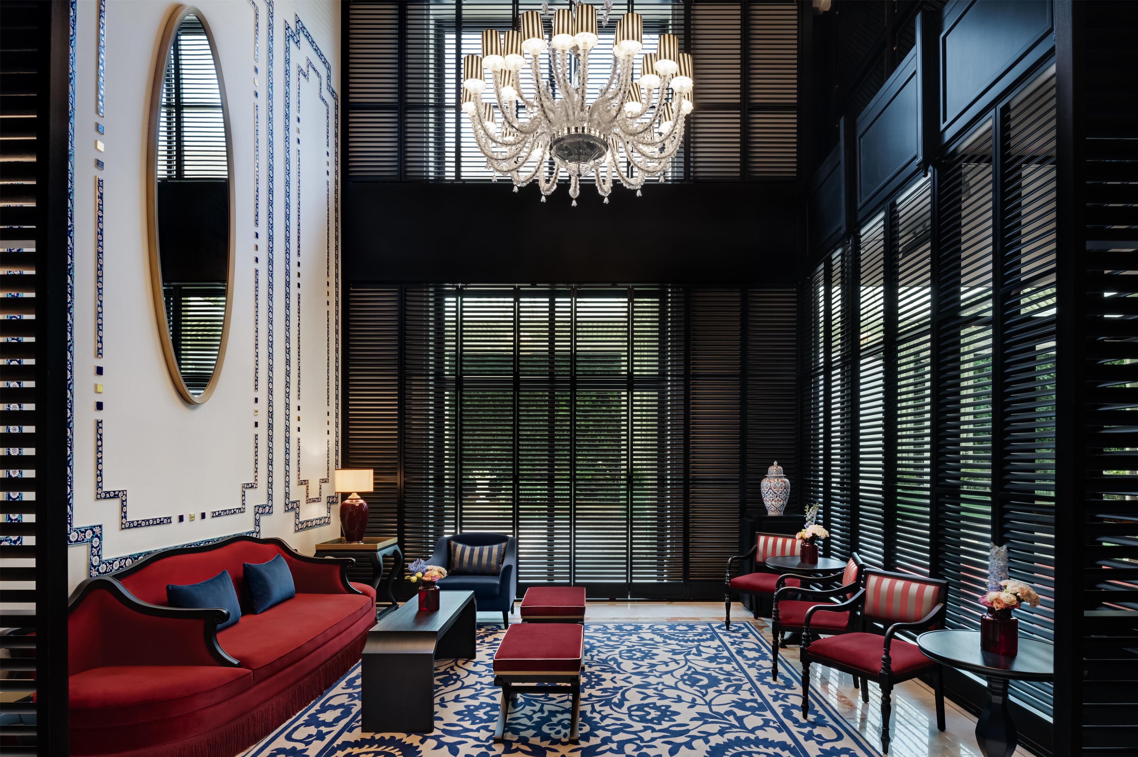 A modern interior with a red sofa, black chairs, a chandelier, and patterned walls.