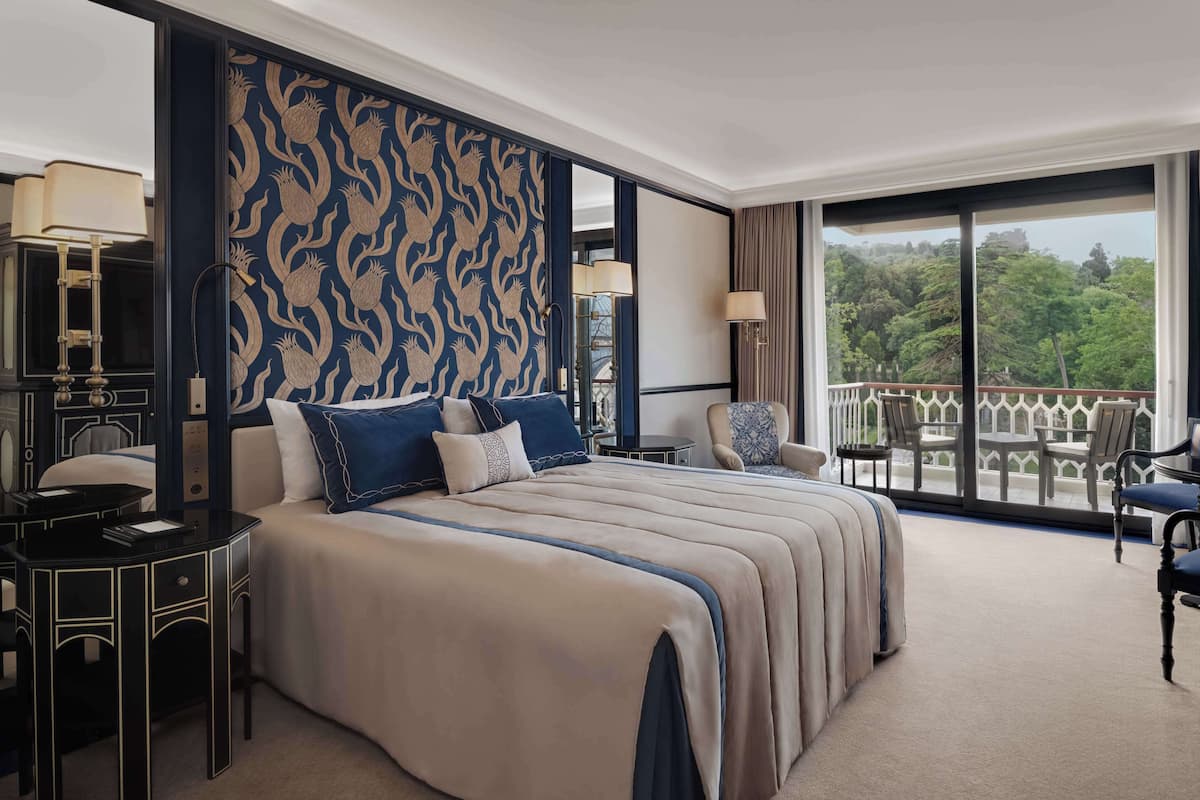A hotel room with a large bed, two bedside tables, a desk, and a balcony with a view of the outdoors.