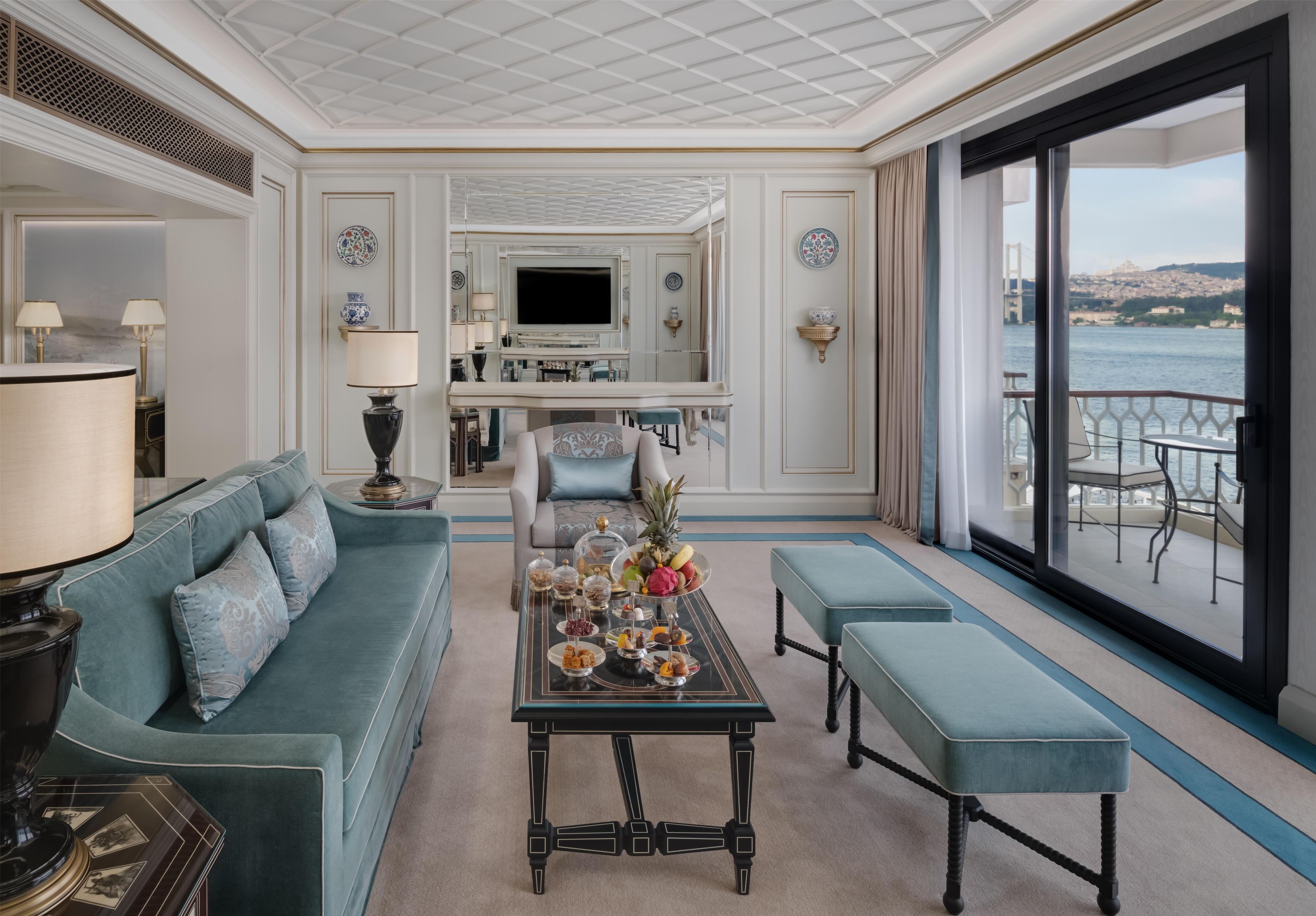 A spacious living area with a sofa, a coffee table with snacks, a TV, and a balcony with a view of a bridge.