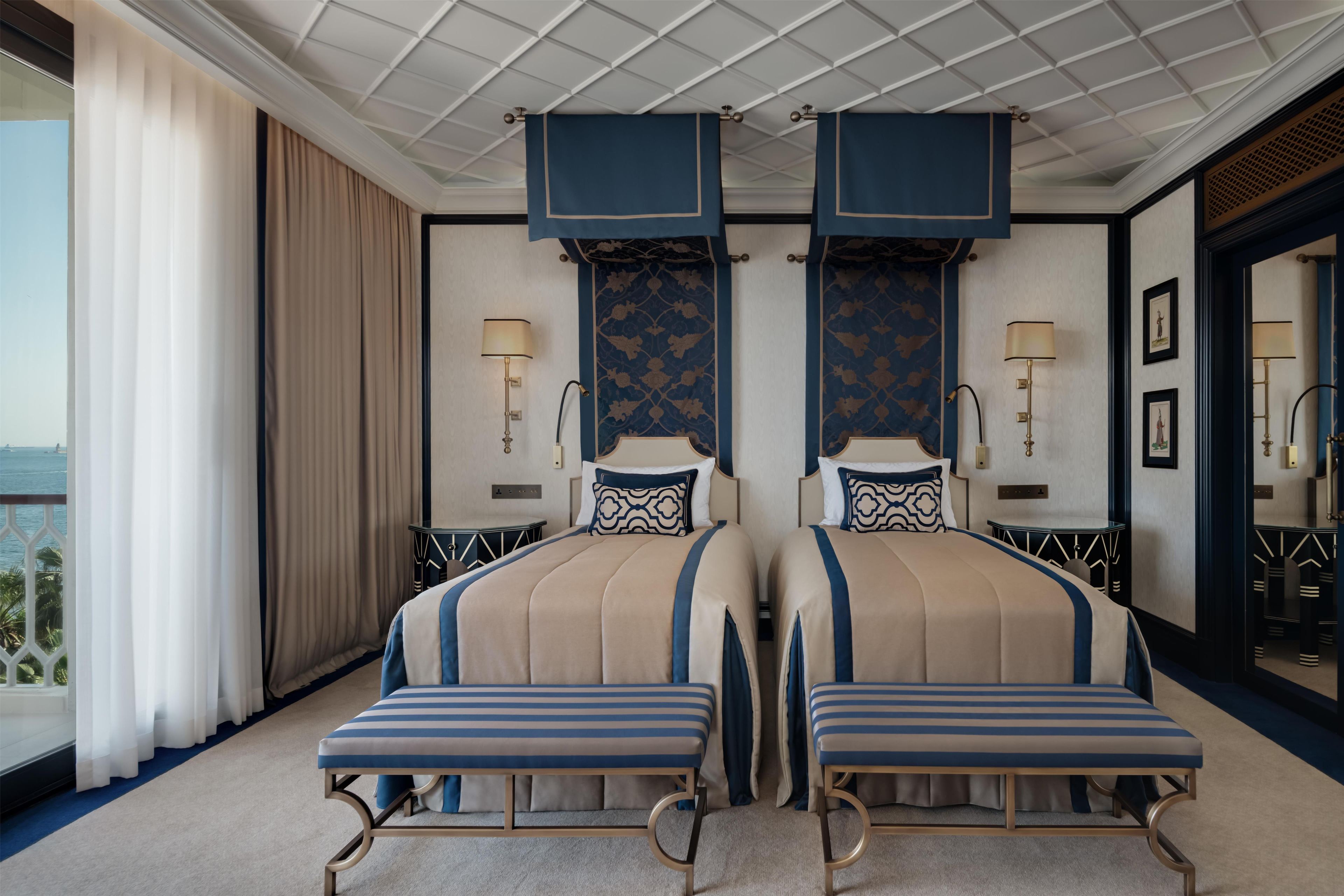 Une chambre d’hôtel avec deux lits, une grande fenêtre avec des rideaux, une vue sur la mer et un balcon.