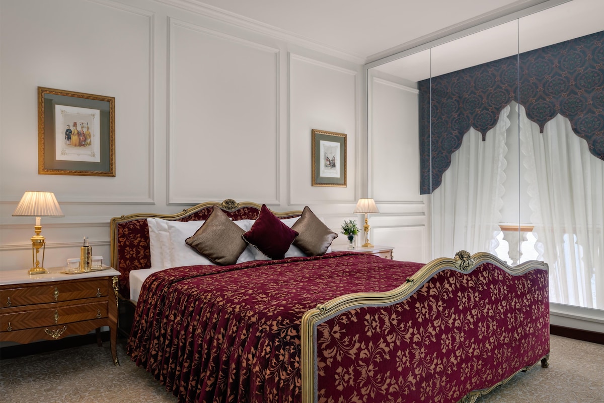 Un dormitorio con una cama grande, dos mesitas de noche, un aparador y un ventanal con cortinas.