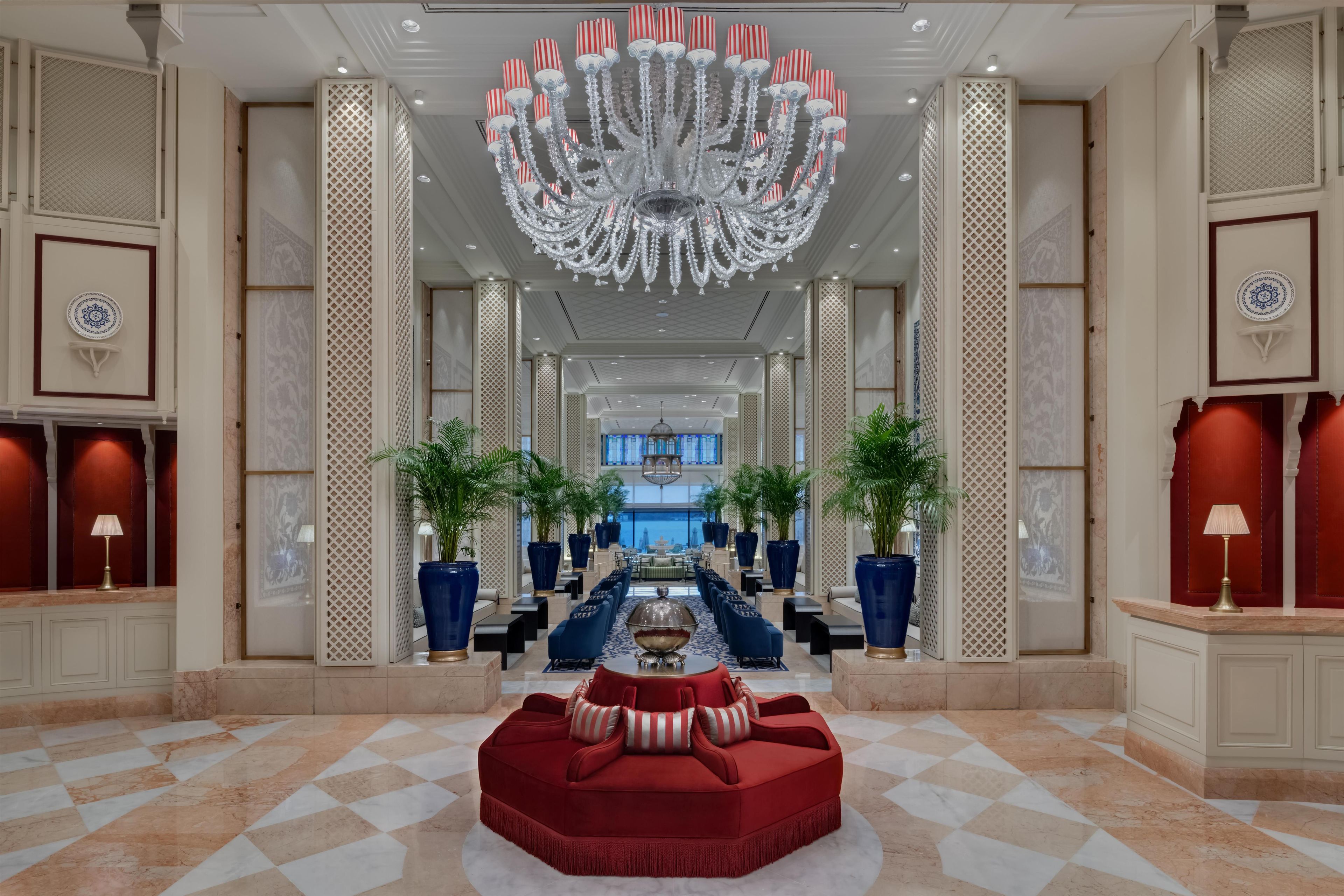 A spacious lobby with a grand chandelier, a red sofa, and a checkered floor.
