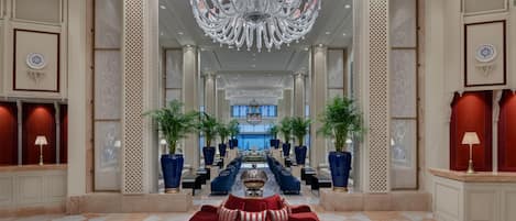 A spacious lobby with a grand chandelier, a red sofa, and a checkered floor.