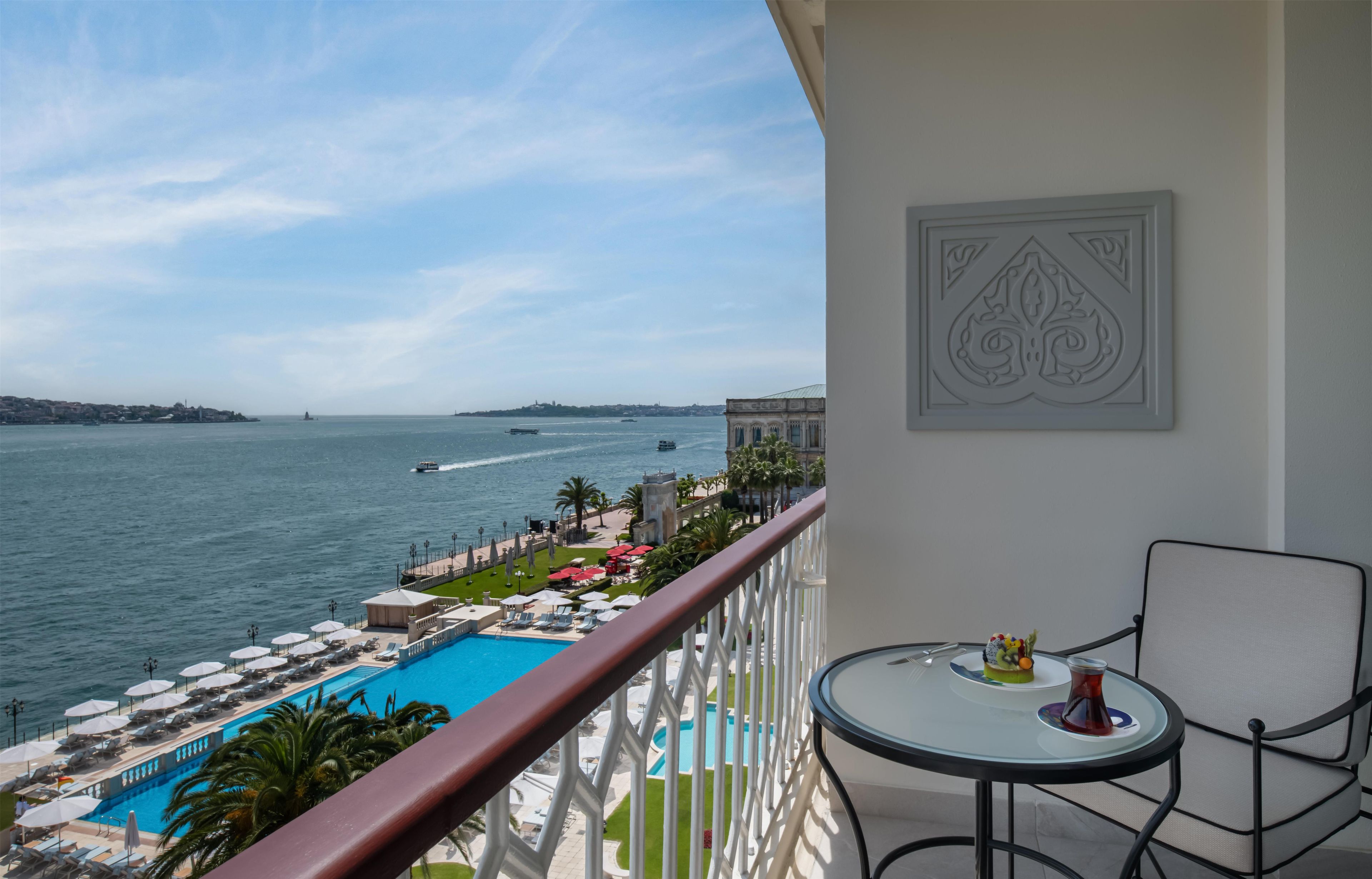 Un balcon avec vue sur une piscine et la mer, une table avec une boisson et un panneau décoratif mural.