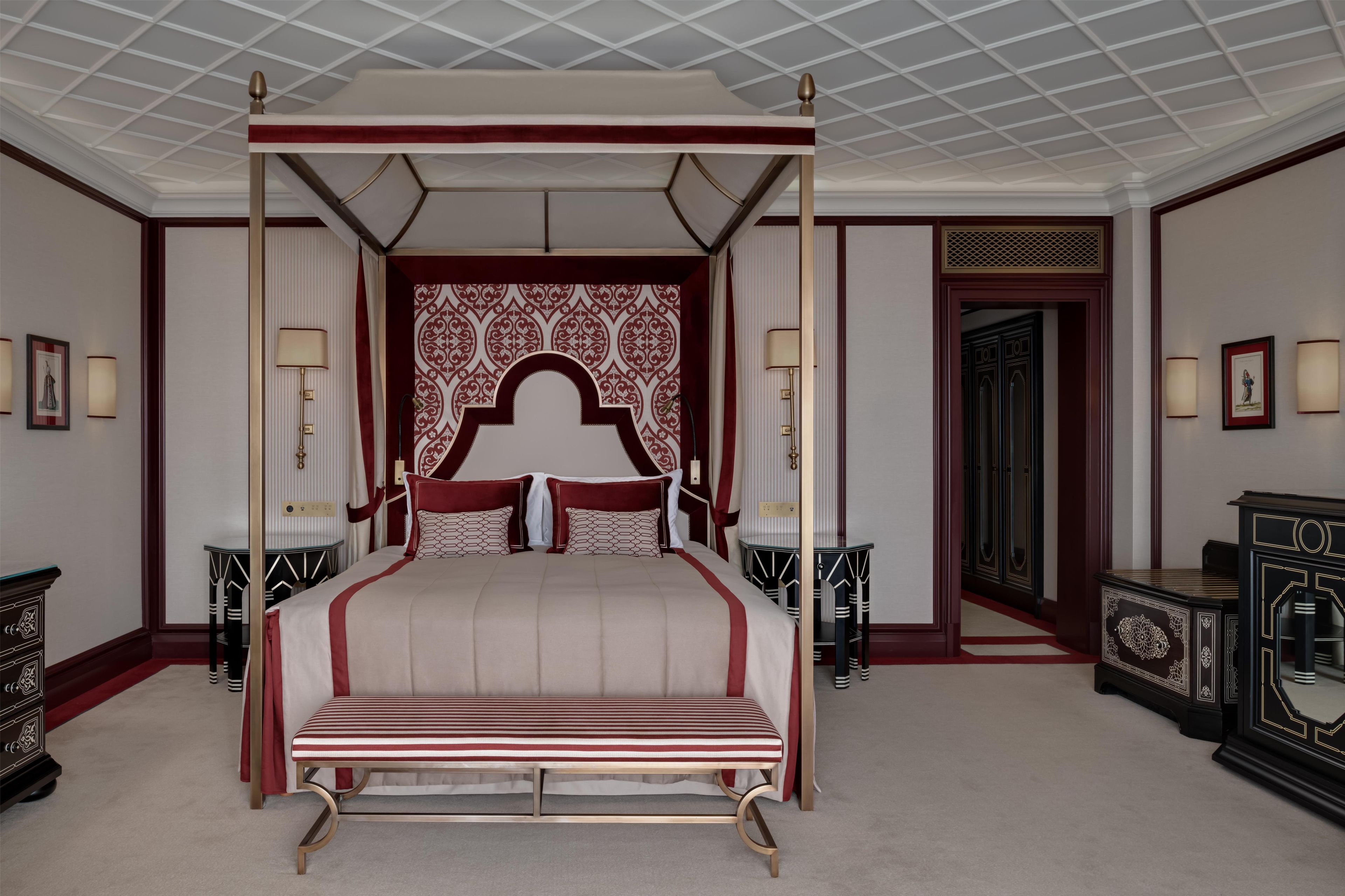 A four-poster bed with a red and white striped bedspread, a red headboard with a decorative pattern, and a canopy overhead.