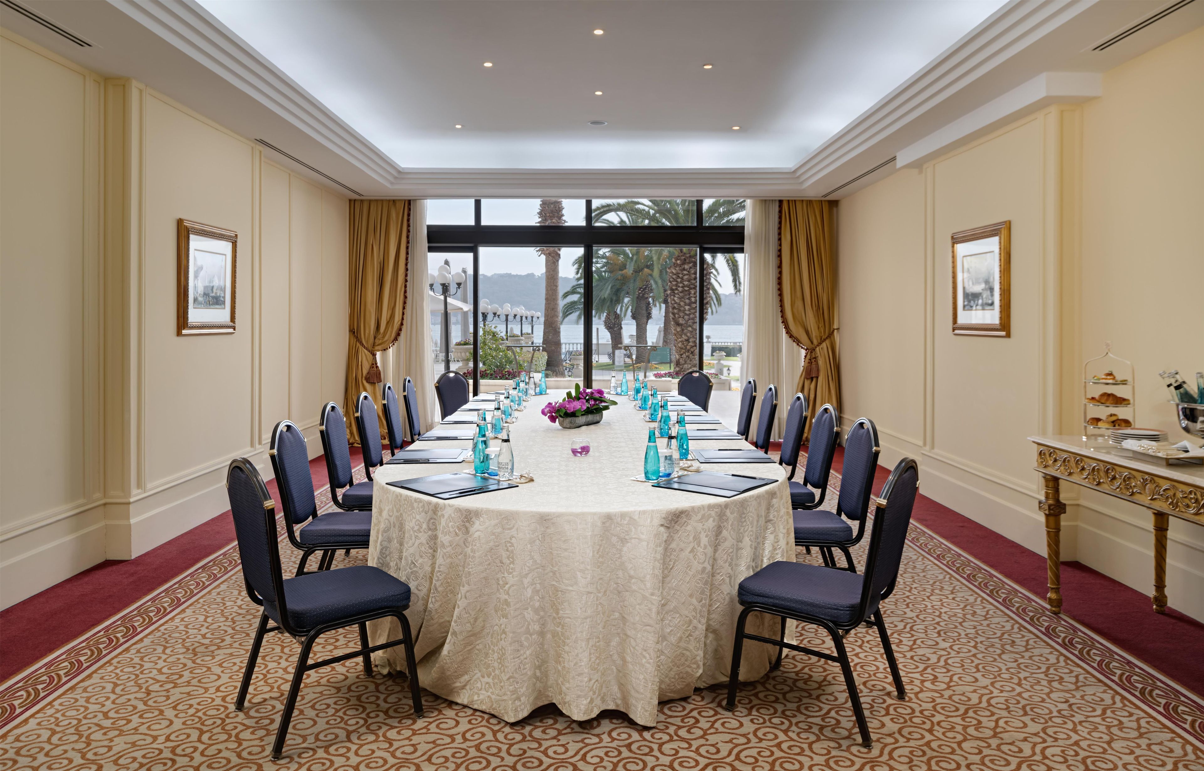 A conference room with a round table, chairs, and a view of the sea through large windows.