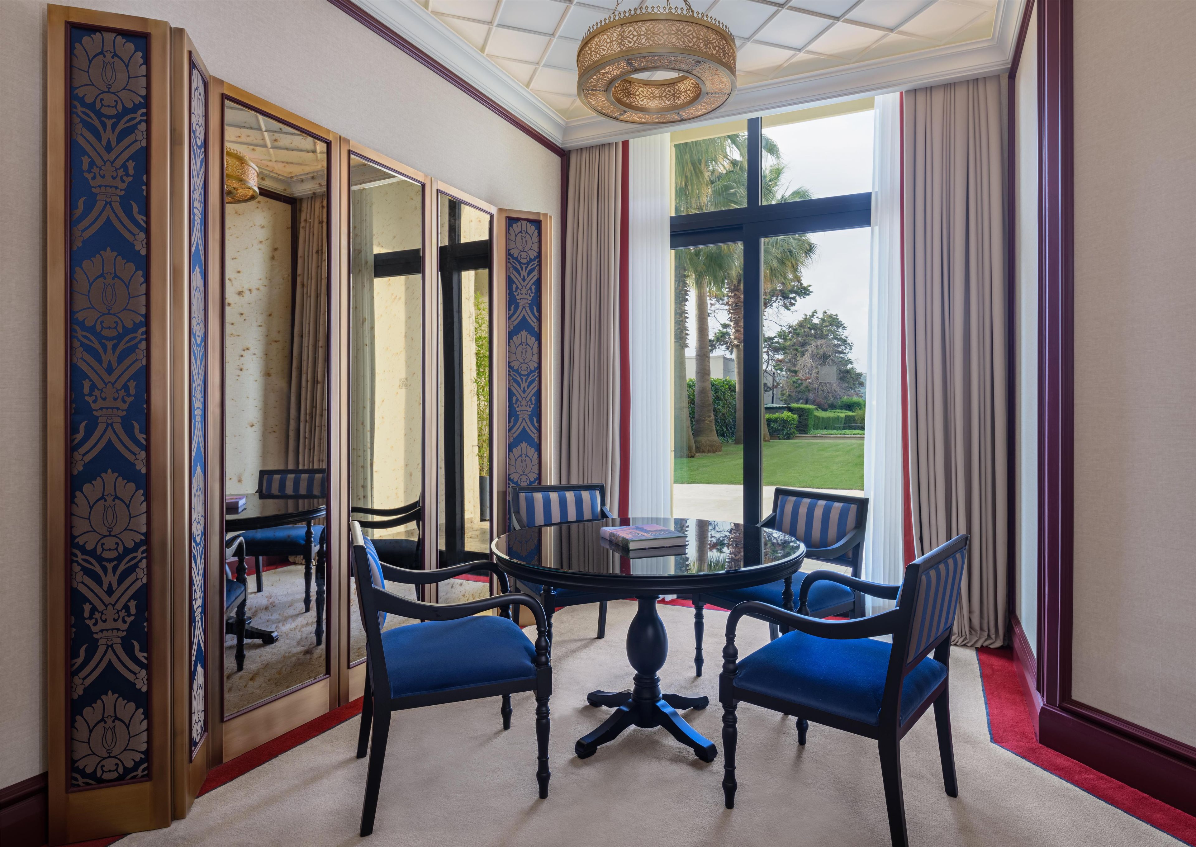 Ein Zimmer mit einem runden Tisch, vier Stühlen, einem großen Spiegel und Blick auf einen Garten.
