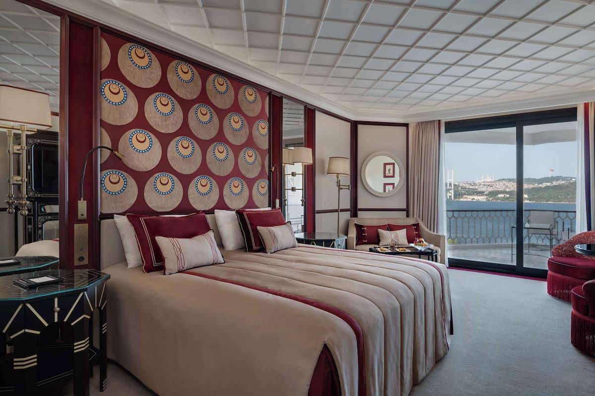 A hotel room with a large bed, a desk, a chair, and a balcony with a view of the city.