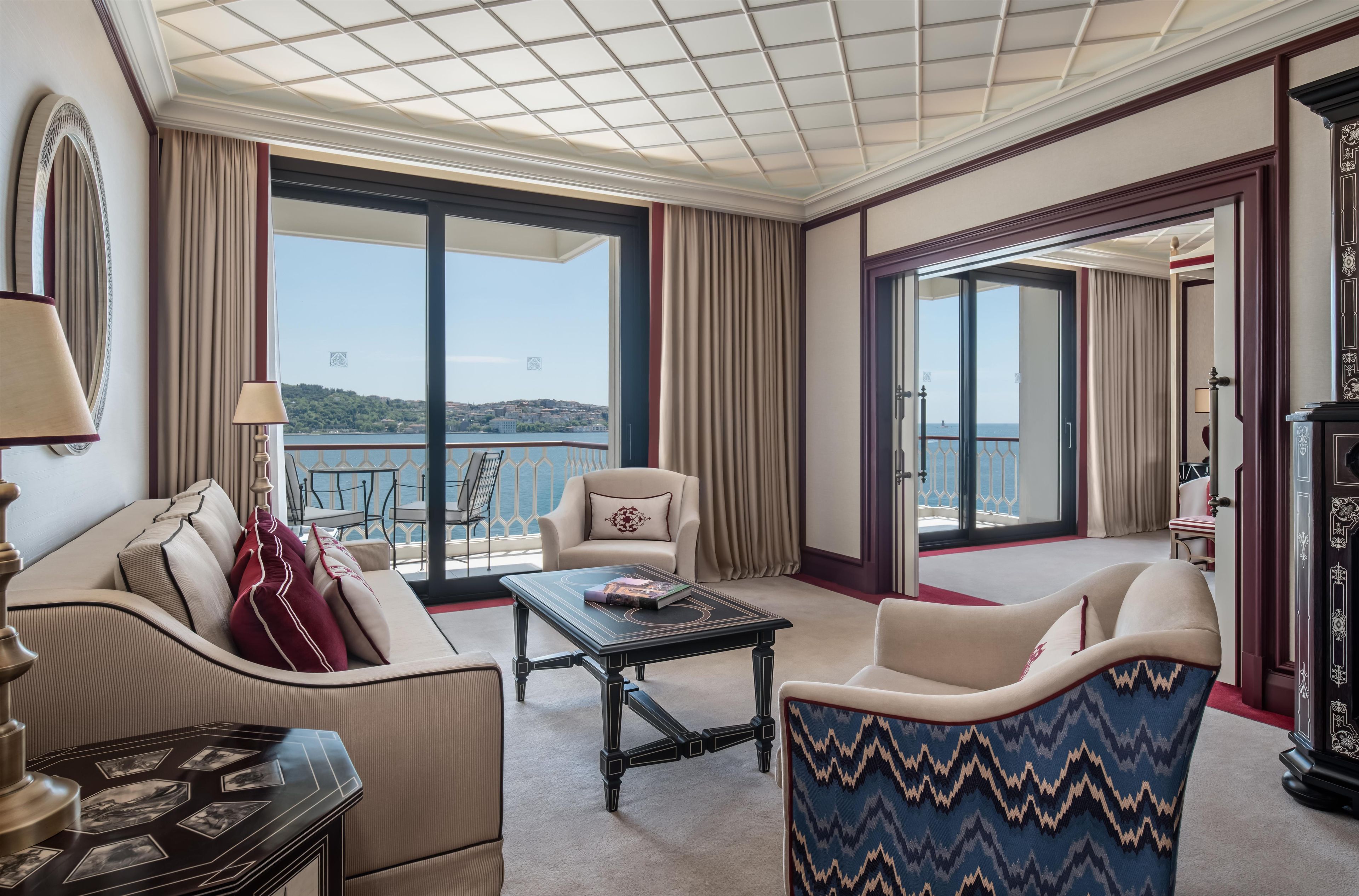 A hotel room with a balcony, a sofa, a chair, a table, and a lamp.