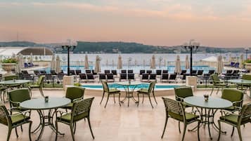 Terraço com área de estar externa e piscina com vista para um corpo de água.
