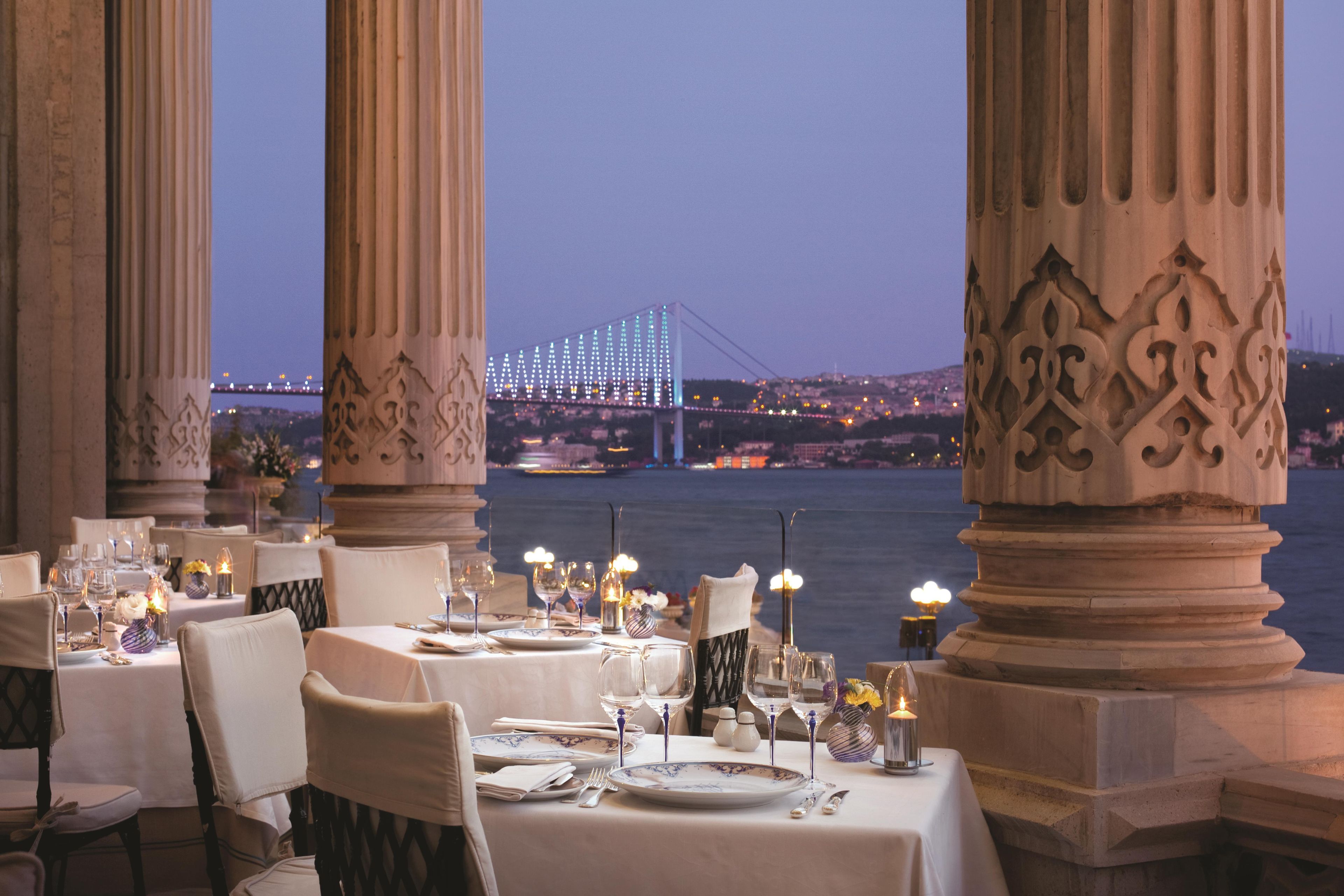 Ein Restaurant mit gedeckten Tischen, mit Blick auf eine Brücke und die Stadt.