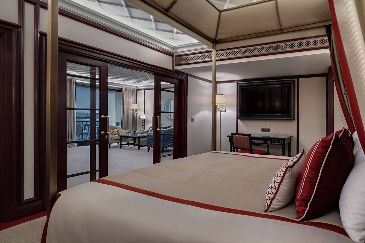 A hotel room with a large bed, a desk with a chair, a television, and a balcony with a view.