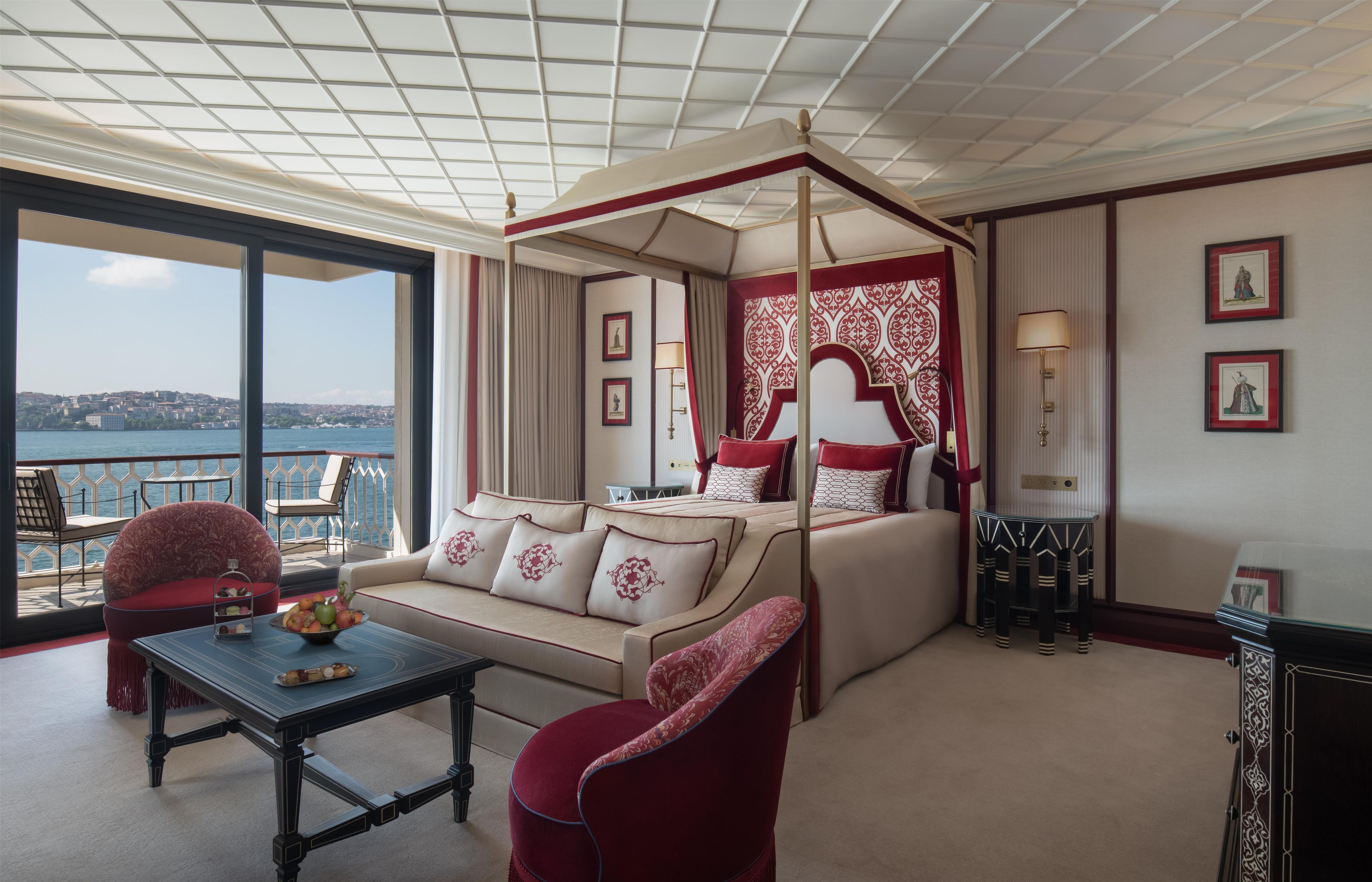 A hotel room with a balcony, a four-poster bed, a sofa, a table, and two chairs.