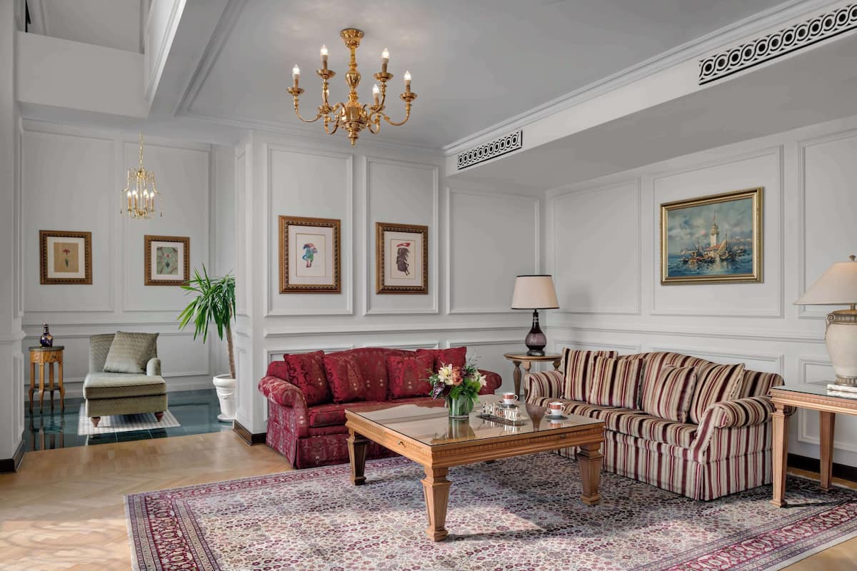 A spacious living room with a red sofa, striped sofa, wooden coffee table, and a chandelier.