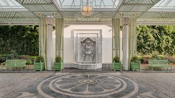 A grand entrance with a marble statue, green benches, and a patterned floor.