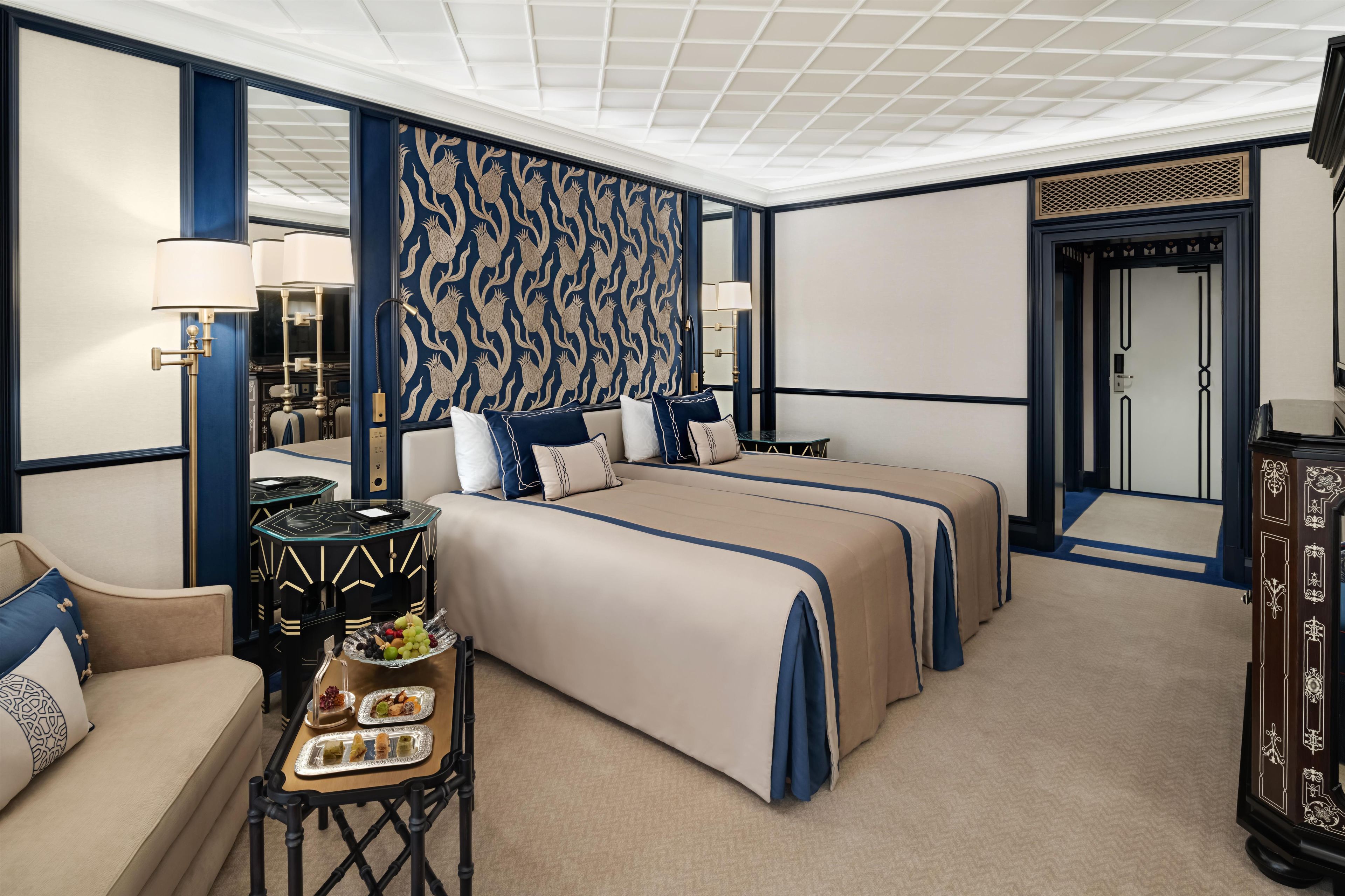 A hotel room with a large bed, a sitting area, a dining table, and a decorative mirror.