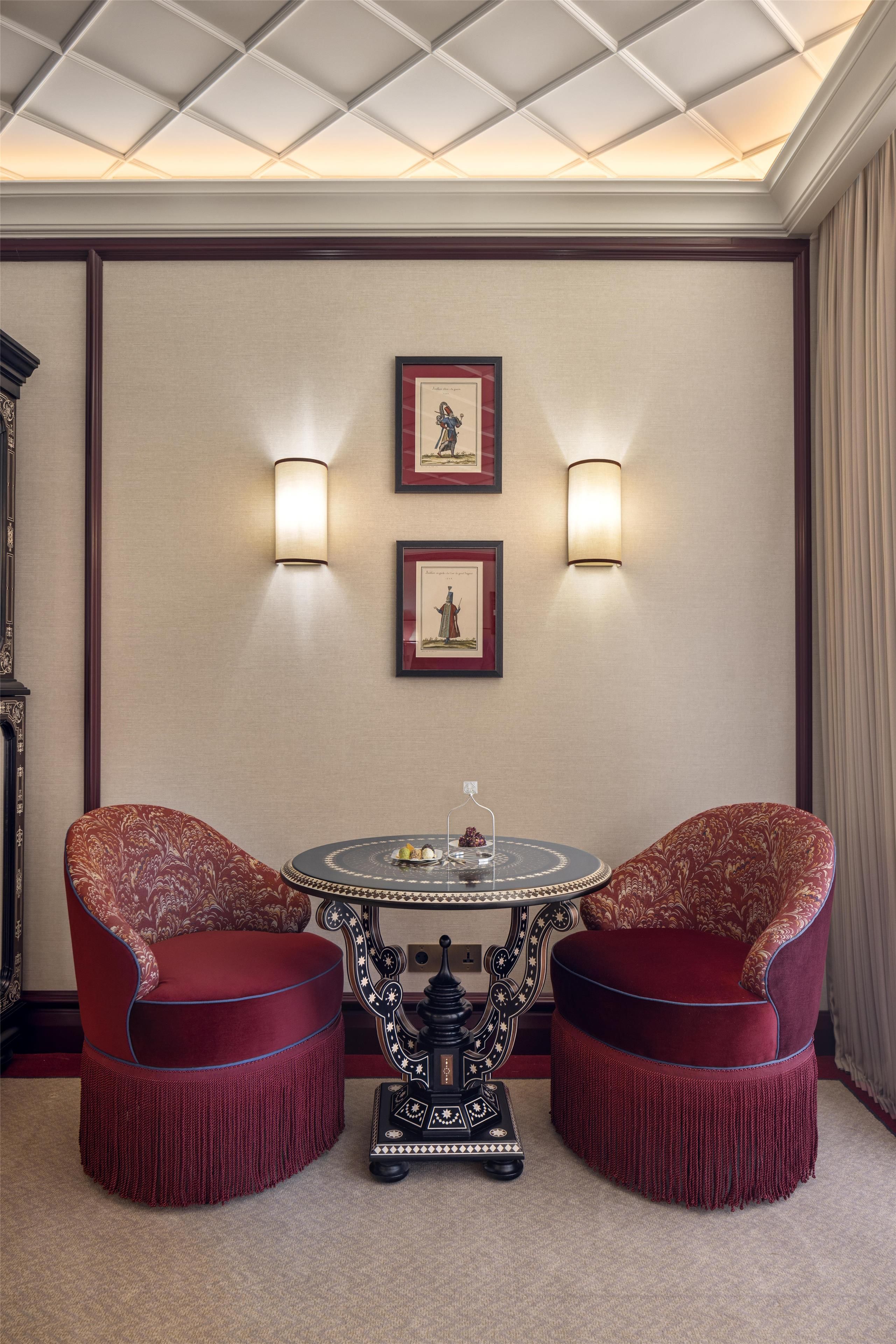 A room with a round table, two chairs, two wall-mounted lights, and two framed pictures.