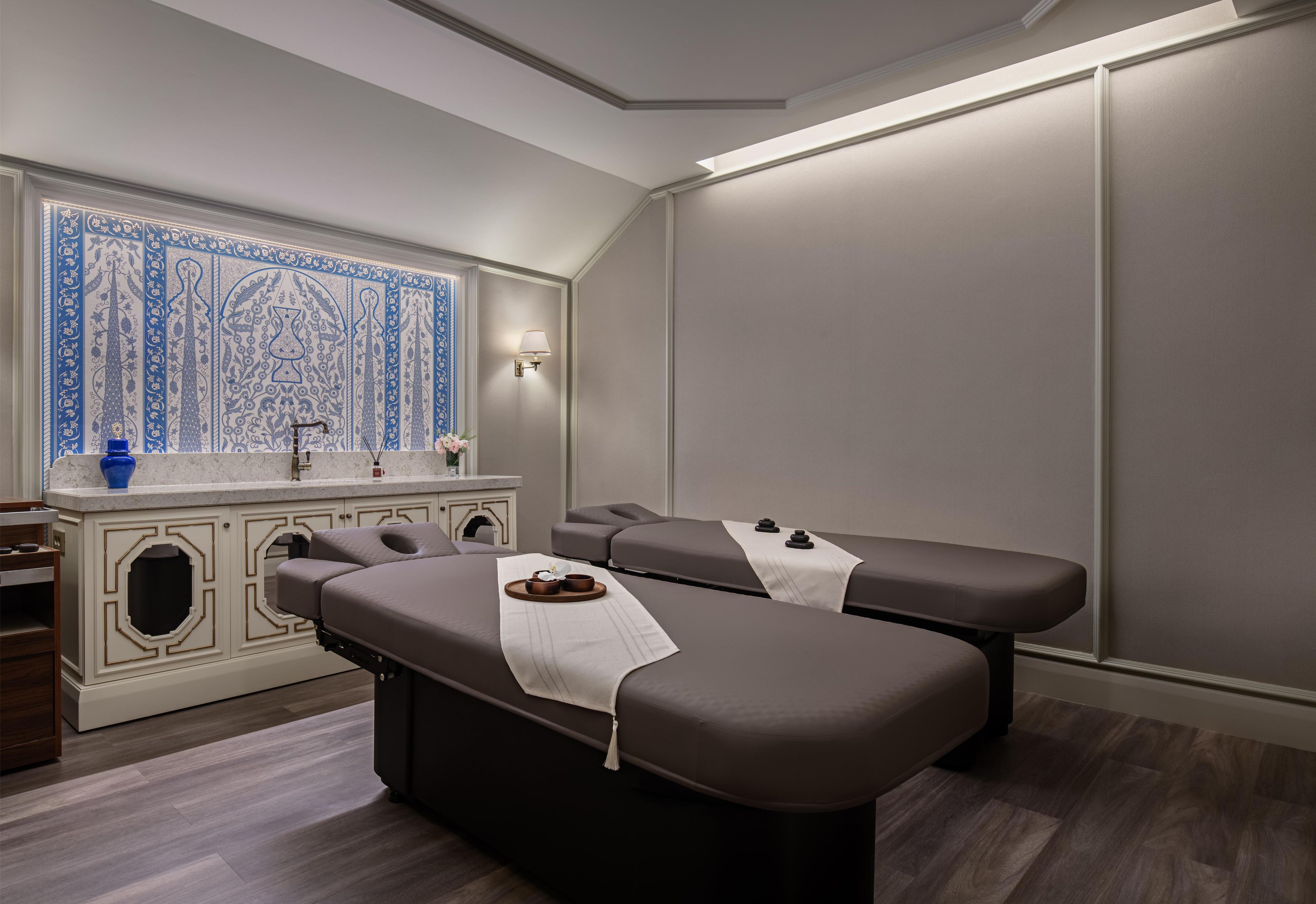 Um spa moderno com duas mesas de massagem, uma parede decorativa com padrões azuis e uma pequena área de lavatório.