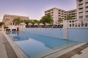 A swimming pool with lounge chairs and umbrellas, surrounded by a high-rise building with balconies. - Ciragan Palace Kempinski (Istanbul)