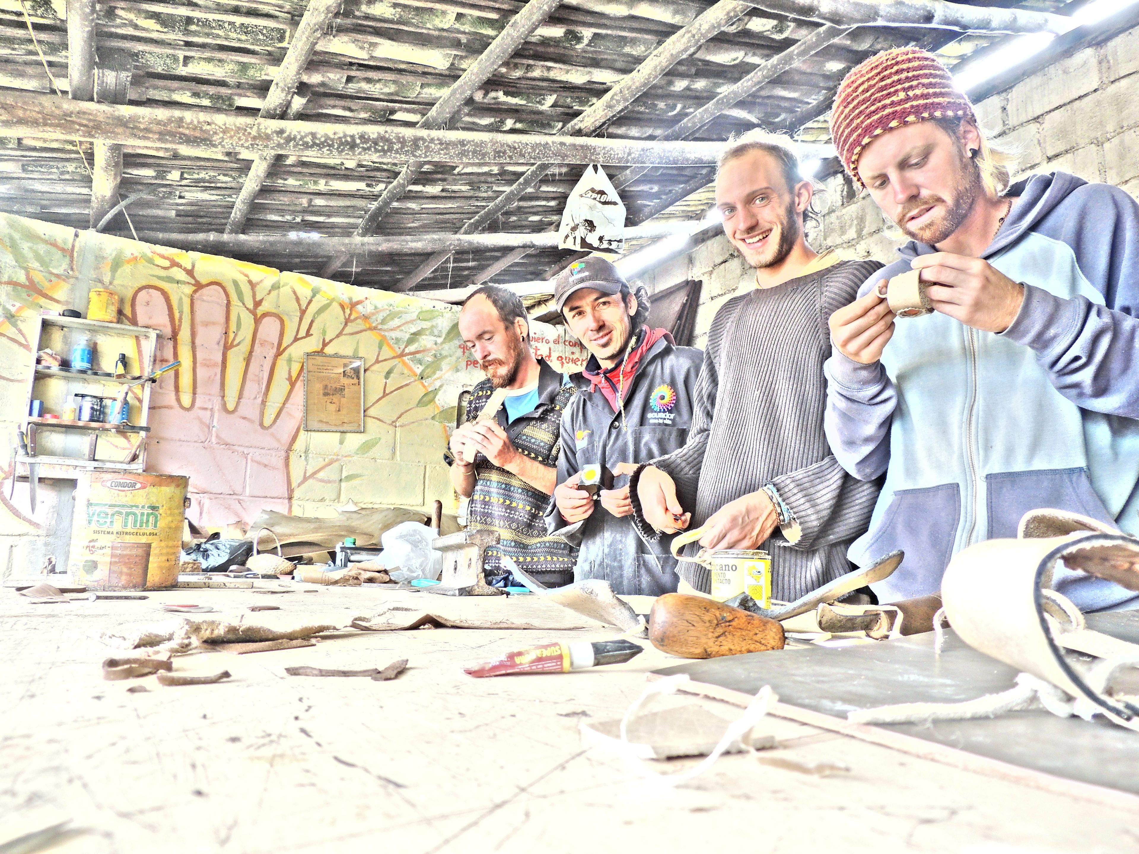 Un taller con herramientas y materiales en el suelo, un mural en la pared y un grupo de personas trabajando.