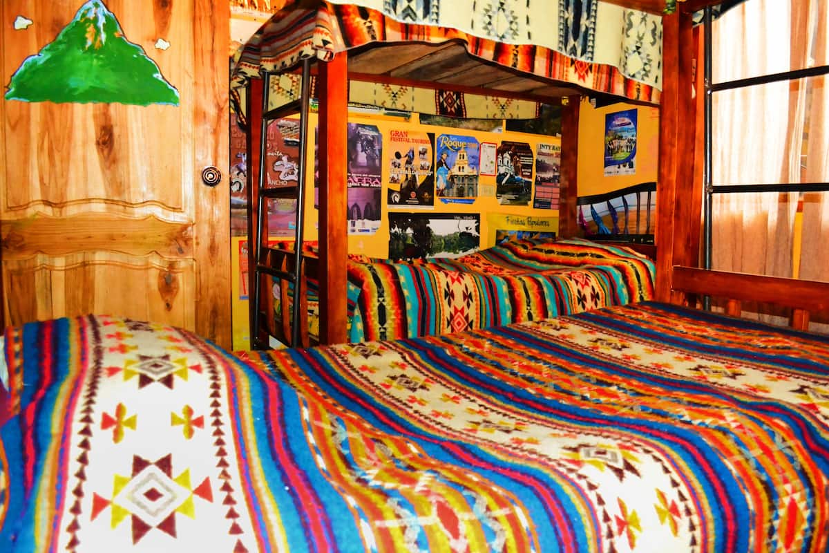Une chambre avec une porte en bois, une literie aux motifs colorés et un mur décoré de divers affiches.