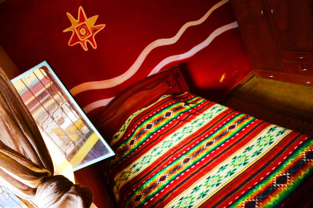 Une chambre avec un lit, un mur décoré de motifs en forme d’étoiles et une fenêtre avec des rideaux.