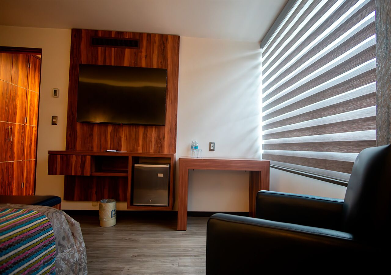 Une chambre d’hôtel avec un lit, un petit bureau, une télévision et une fenêtre avec des stores.