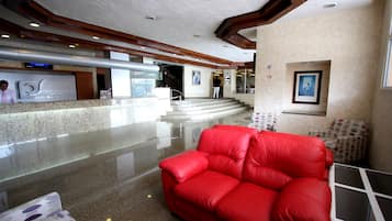 A hotel lobby with a red leather sofa, a reception desk, and a staircase leading to upper floors.