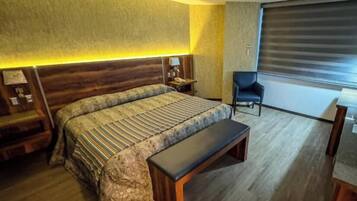 Habitación de hotel con una cama grande, un banco, un escritorio y una silla.