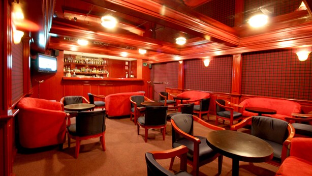 A bar area with red and black furniture, a bar counter, and a television screen. - Hotel Parque Satelite (Tlalnepantla de Baz)