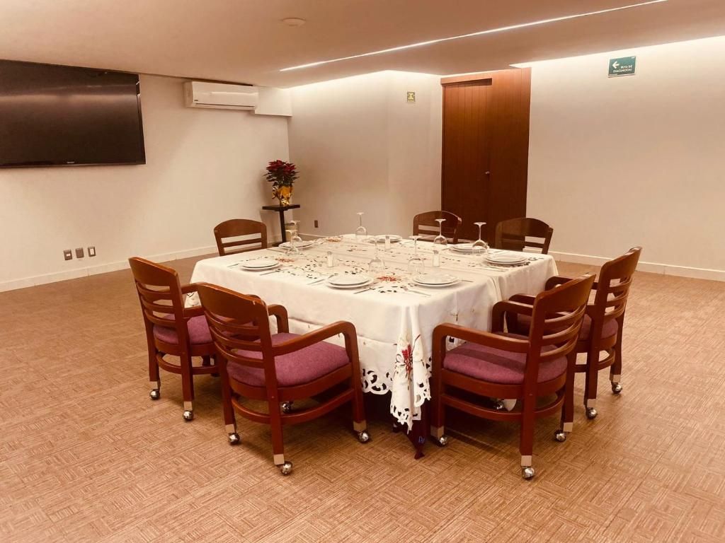 A conference room with a round table, eight wooden chairs with cushioned seats, and a white tablecloth.