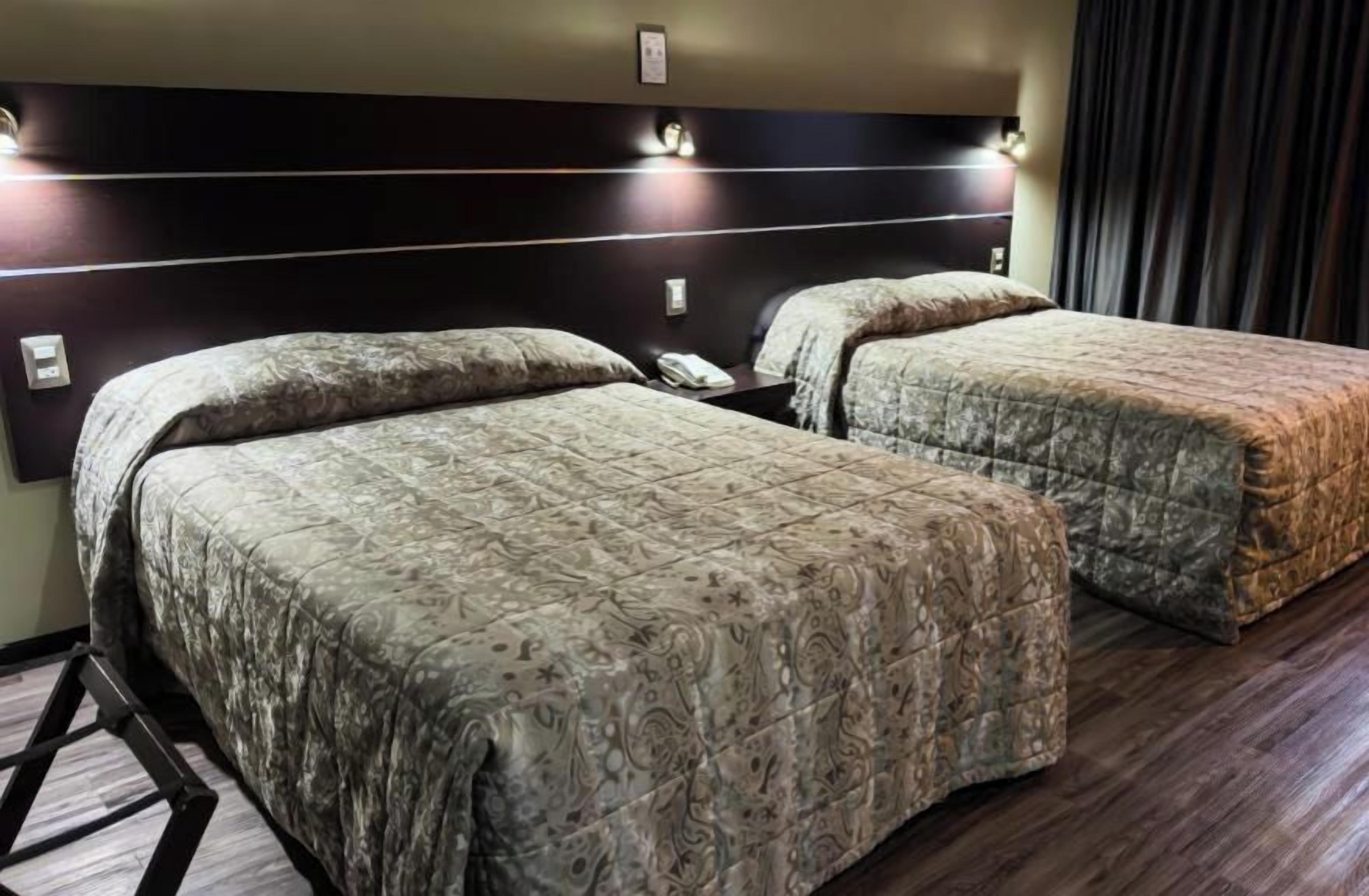 A hotel room with two beds, a dark headboard, and a wooden floor.