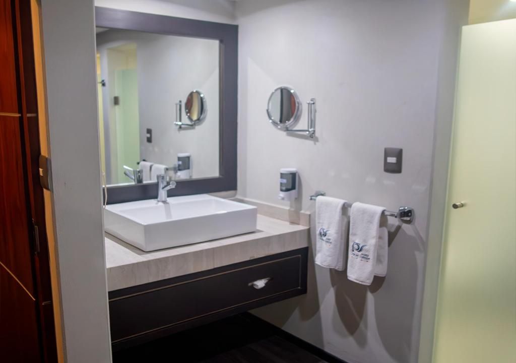 A modern bathroom with a large mirror, a white sink, and a towel rack with two towels.