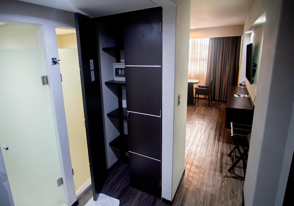Habitación de hotel con distribución compacta, que incluye una kitchenette con microondas, un pequeño rincón de estar con una mesa y sillas, y un televisor montado en la pared.