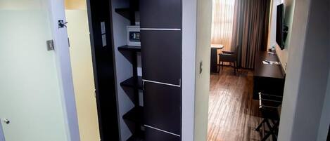 A hotel room with a compact layout, including a kitchenette with a microwave, a small seating area with a table and chairs, and a television mounted on the wall.
