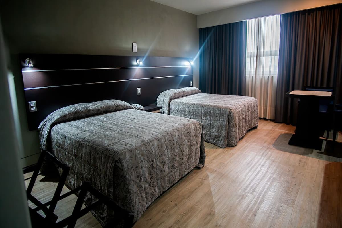 A hotel room with two beds, a desk, and a large window with curtains.