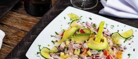 Prato branco com salada de frutos do mar sobre mesa escura e texturizada.