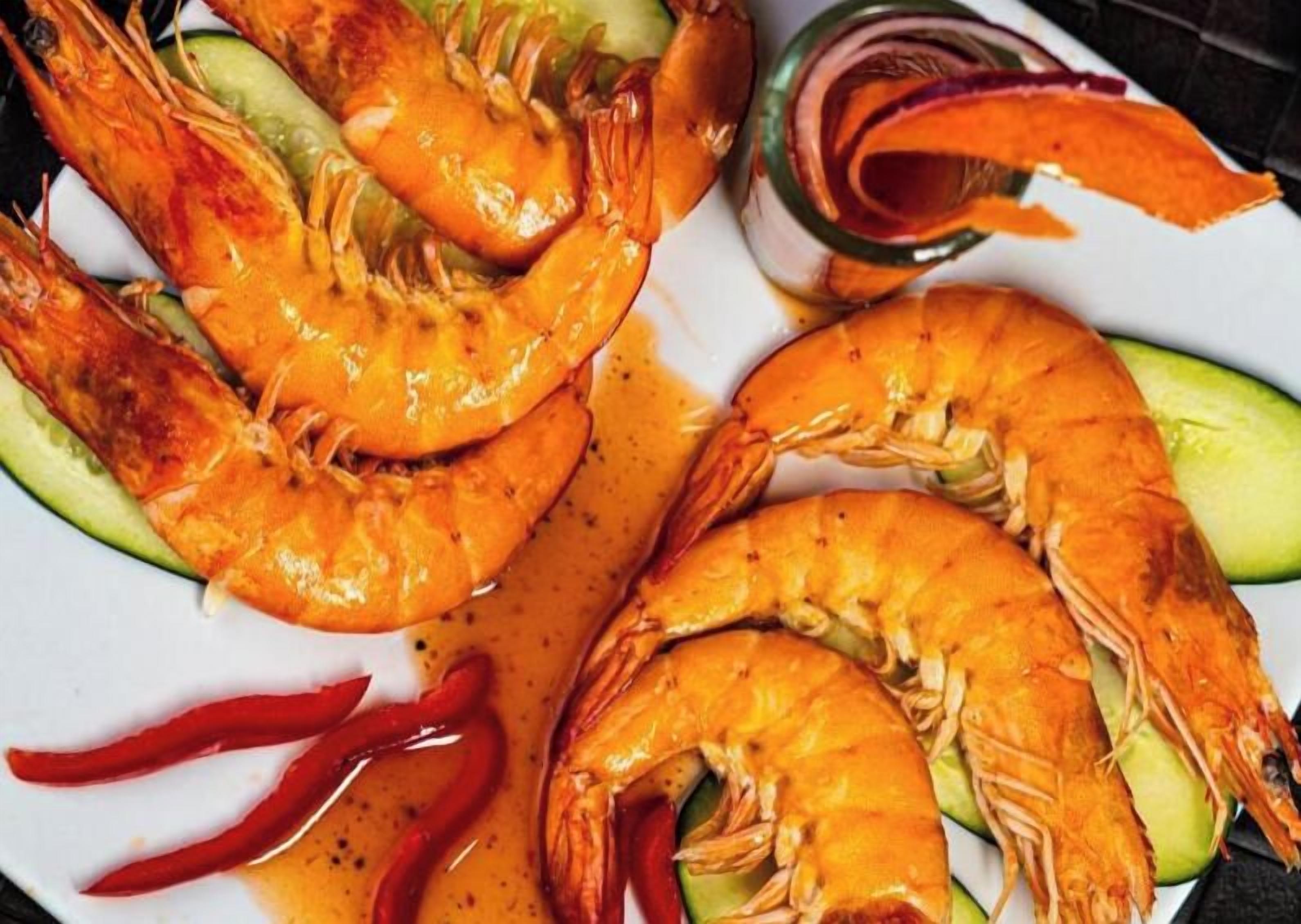 A plate of cooked shrimp with slices of cucumber and red chili peppers.