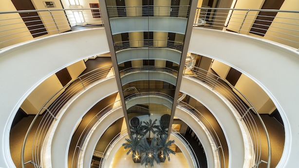 A multi-level atrium with a central glass elevator shaft, multiple balconies, and a decorative palm tree sculpture.