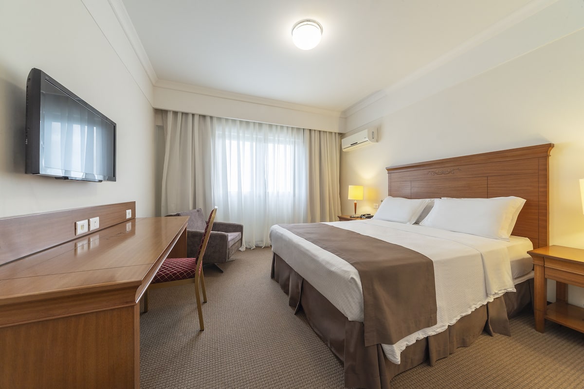 Une chambre d’hôtel équipée d’un lit, d’un bureau, d’une chaise, d’une télévision et d’une fenêtre avec des rideaux.