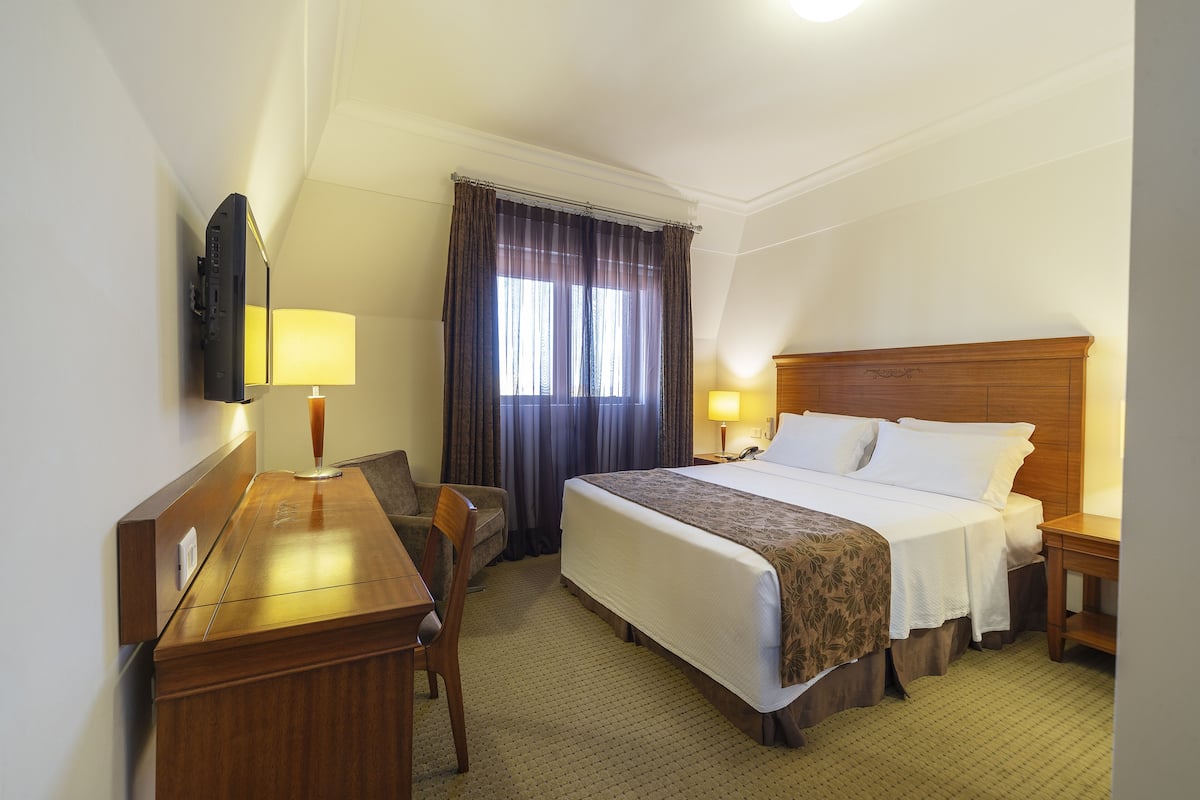 Une chambre d’hôtel équipée d’un lit, d’un bureau, d’une chaise, d’un téléviseur fixé au mur et d’une fenêtre avec des rideaux.
