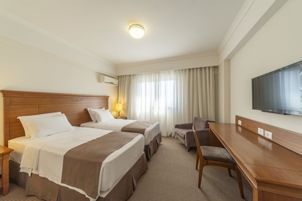 Une chambre d’hôtel avec deux lits, un bureau, une chaise, une télévision et une fenêtre avec des rideaux.