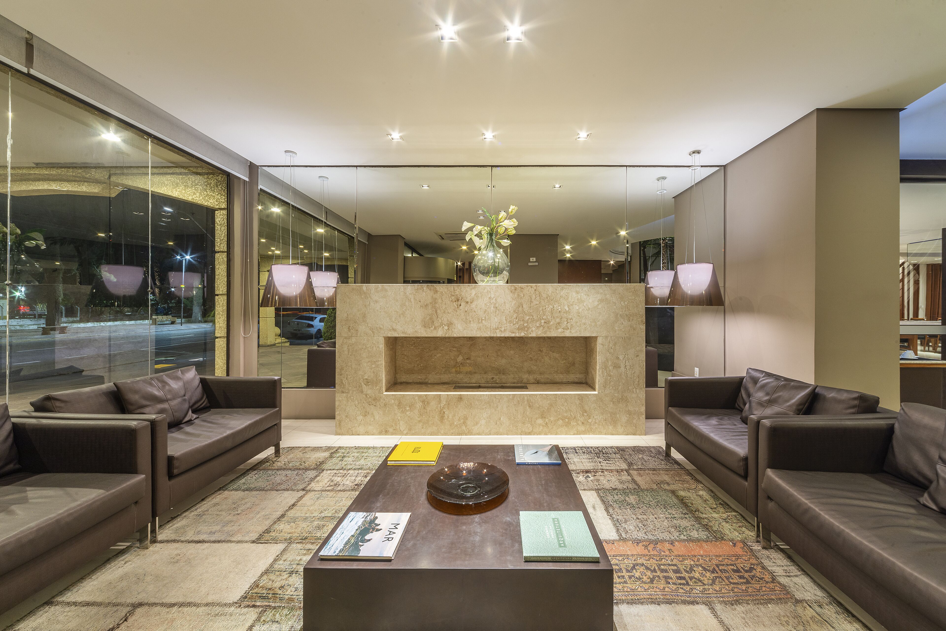 A modern lobby with a central fireplace, sofas, and a coffee table with books.