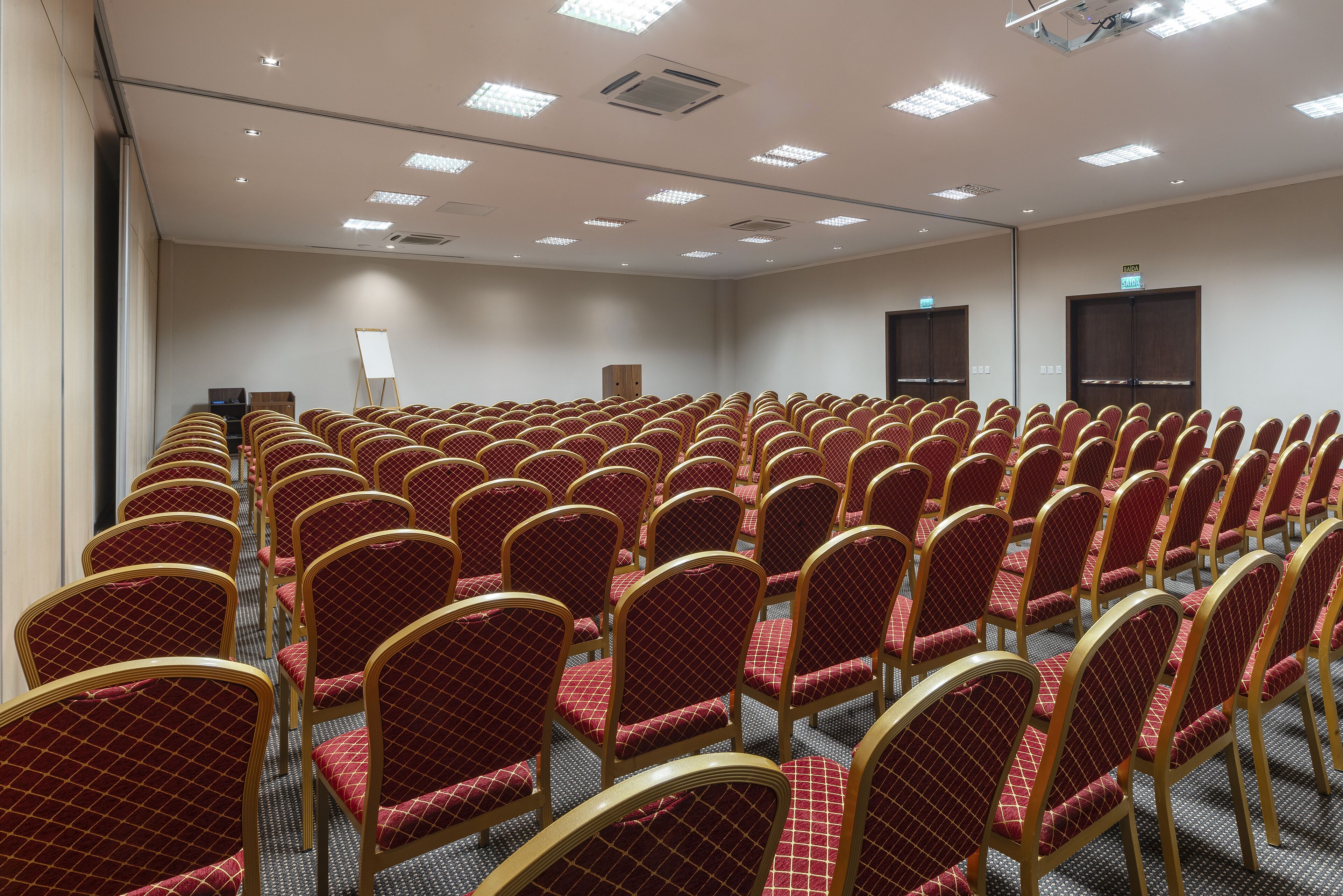 Un salón de conferencias con filas de sillas tapizadas en rojo y un atril al frente.
